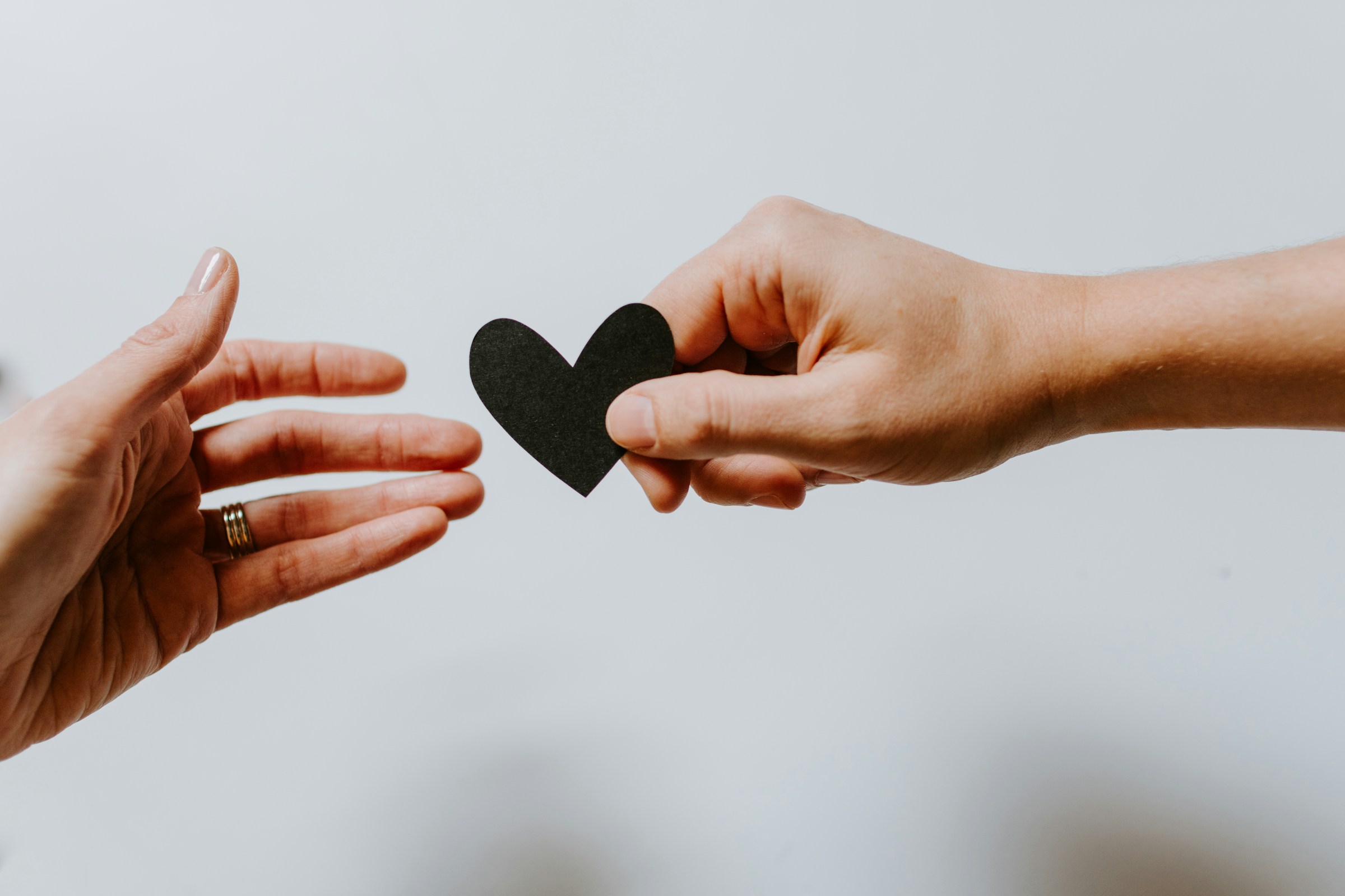 A hand handing a black, paper heart to another hand